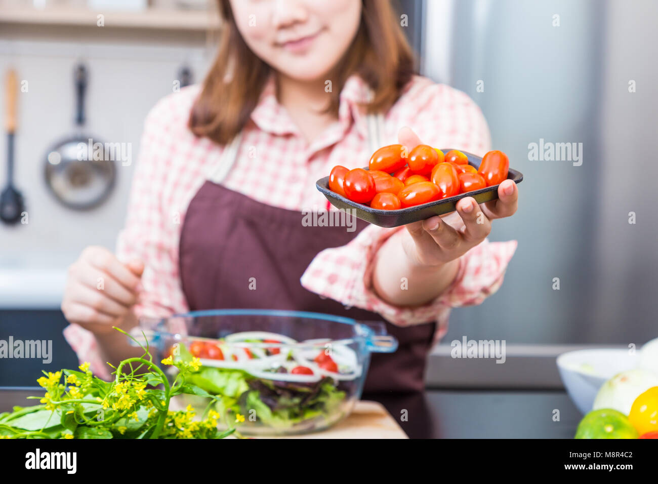 Giovani felici cuoca tenendo fuori un pacjage o pomodori rossi verso la telecamera, il fuoco selettivo per la buona cucina salutare dieta o tema Foto Stock
