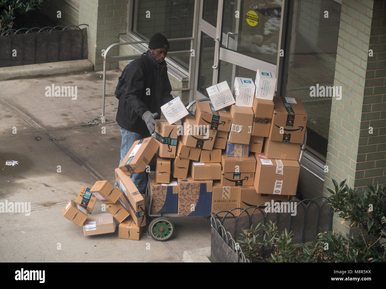 Un deliveryman da Lasership con il suo carrello carico di acquisti da personaggi del calibro di Amazon, grembiule blu e altri tipi le proprie consegne a un palazzo di appartamenti quartiere di Chelsea di New York venerdì 9 marzo, 2018 . (© Richard B. Levine) Foto Stock