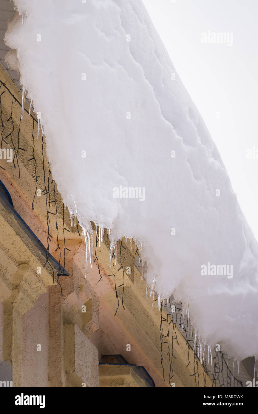Enorme neve pericolose e ghiacciolo formazione sul tetto. Pericolo di fusione del ghiaccio sospesi dal tetto di un vecchio edificio in inverno Foto Stock