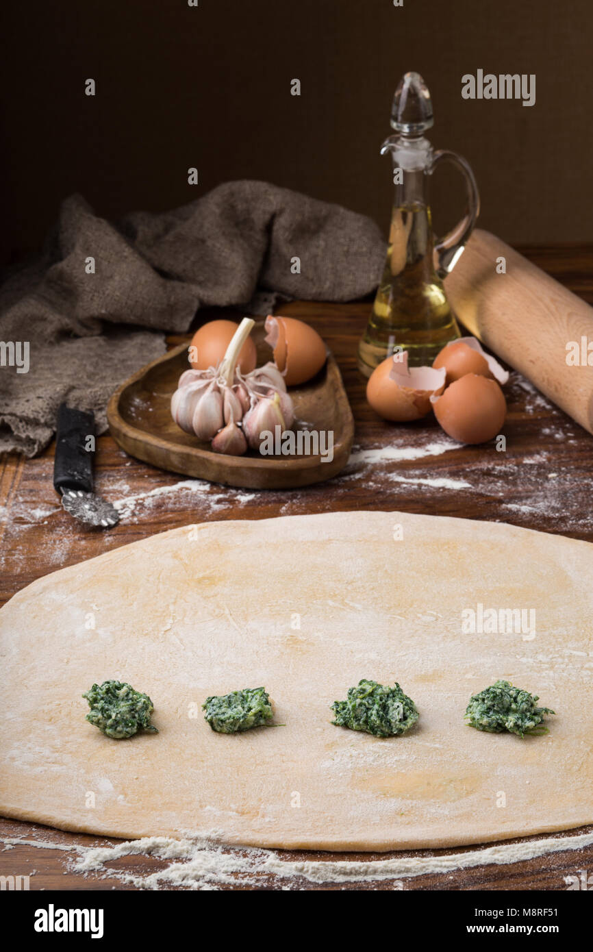 La tazza di farina, le uova, il matterello, olio d'oliva in un recipiente su un sfondo di legno, rendendo i ravioli. Foto Stock