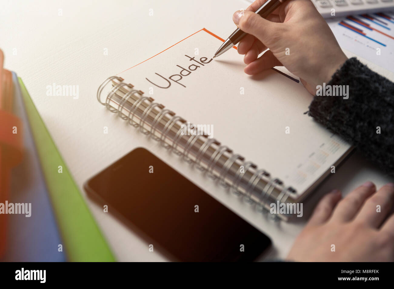 Womans la scrittura a mano parola aggiornamento in un portatile su una scrivania. Aggiornamento sul progetto checklist. Notebook, penna e libri. Aggiornamento del sistema Foto Stock