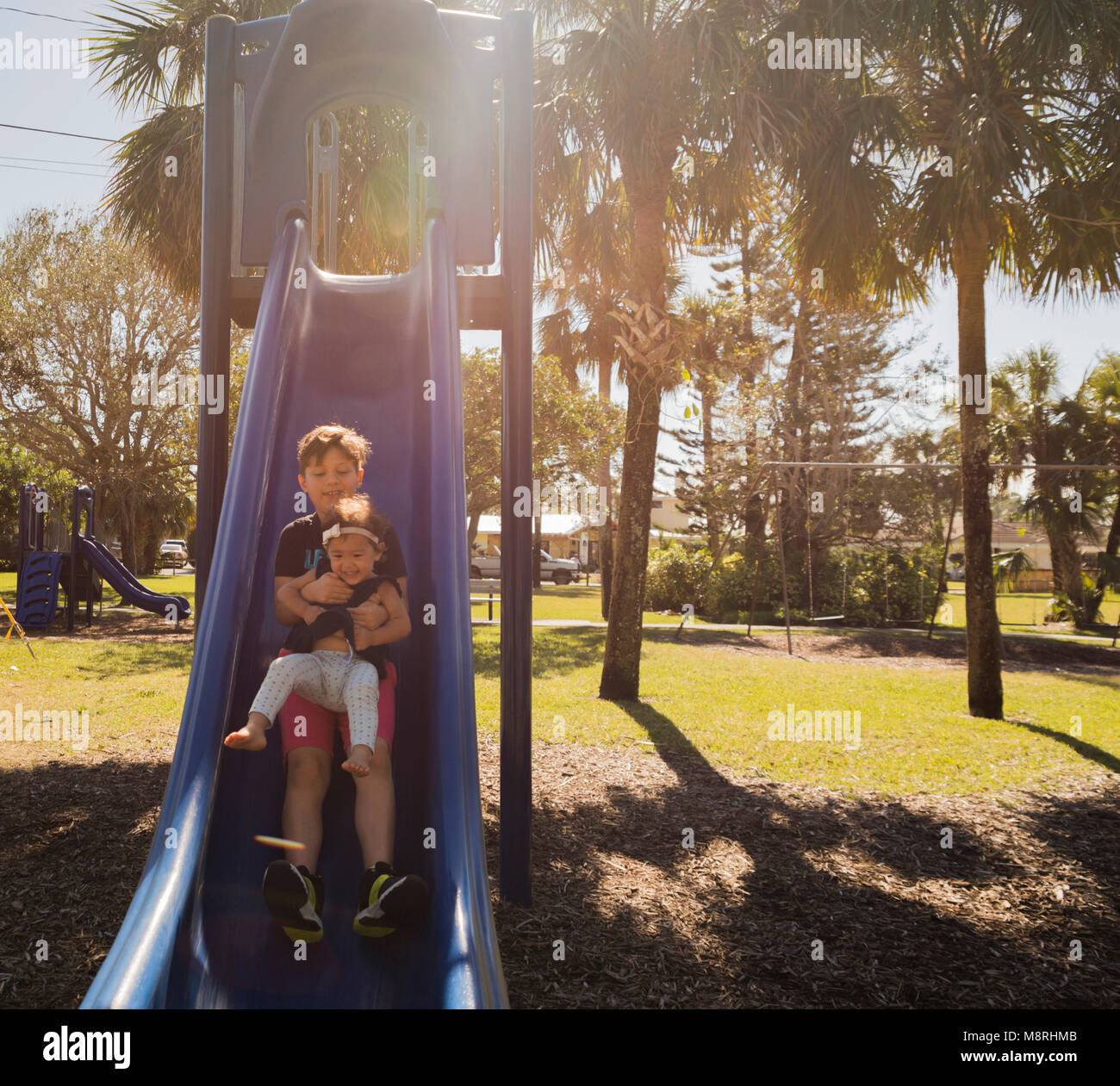 Fratello con la sorella scorrevole sulla slitta al parco giochi durante la giornata di sole Foto Stock