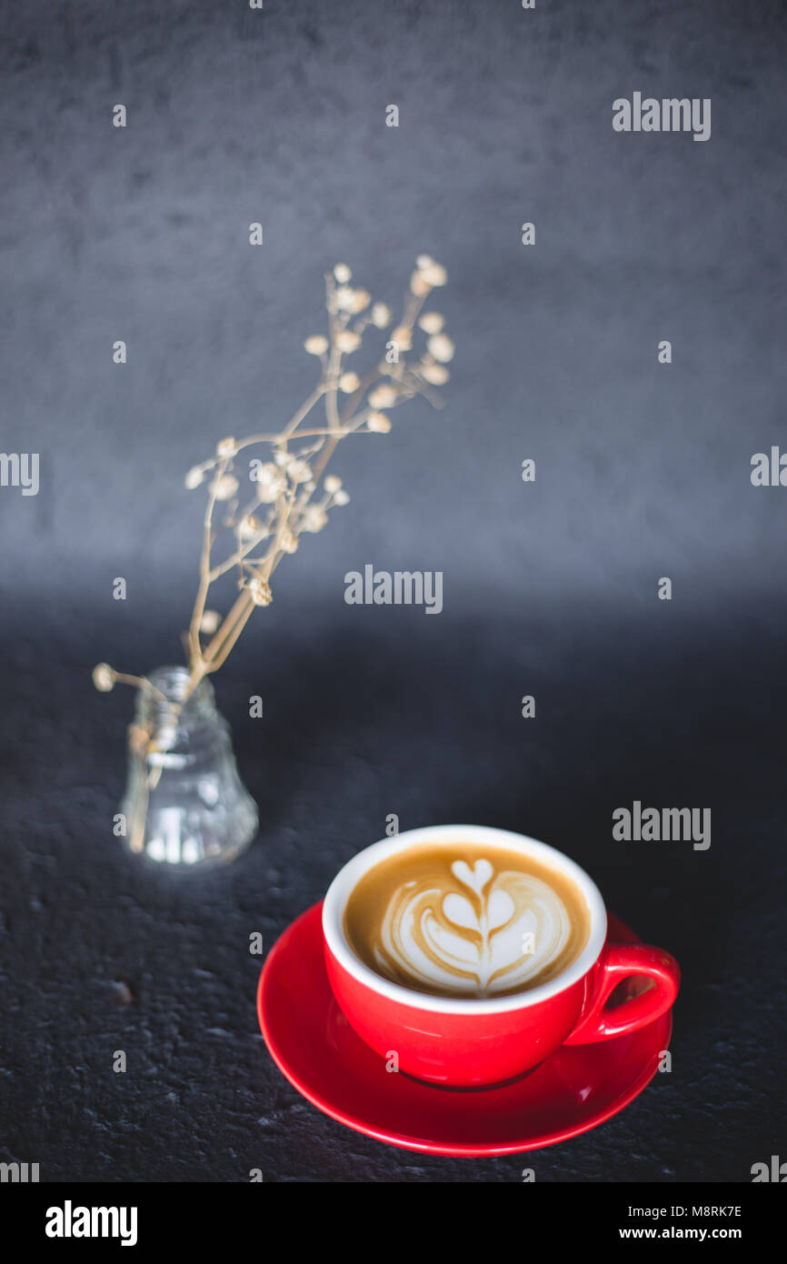 Un rosso tazza di caffè latte ' ' su uno spazio nero con fiori secchi Foto Stock
