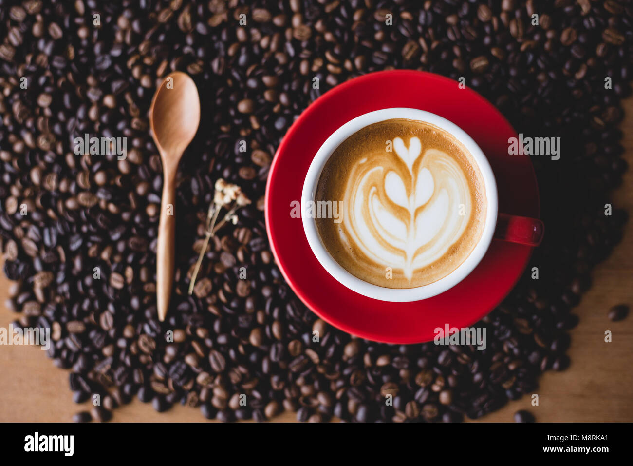 Un rosso tazza di caffè latte ' ' sul chicco di caffè con il cucchiaio di legno Foto Stock