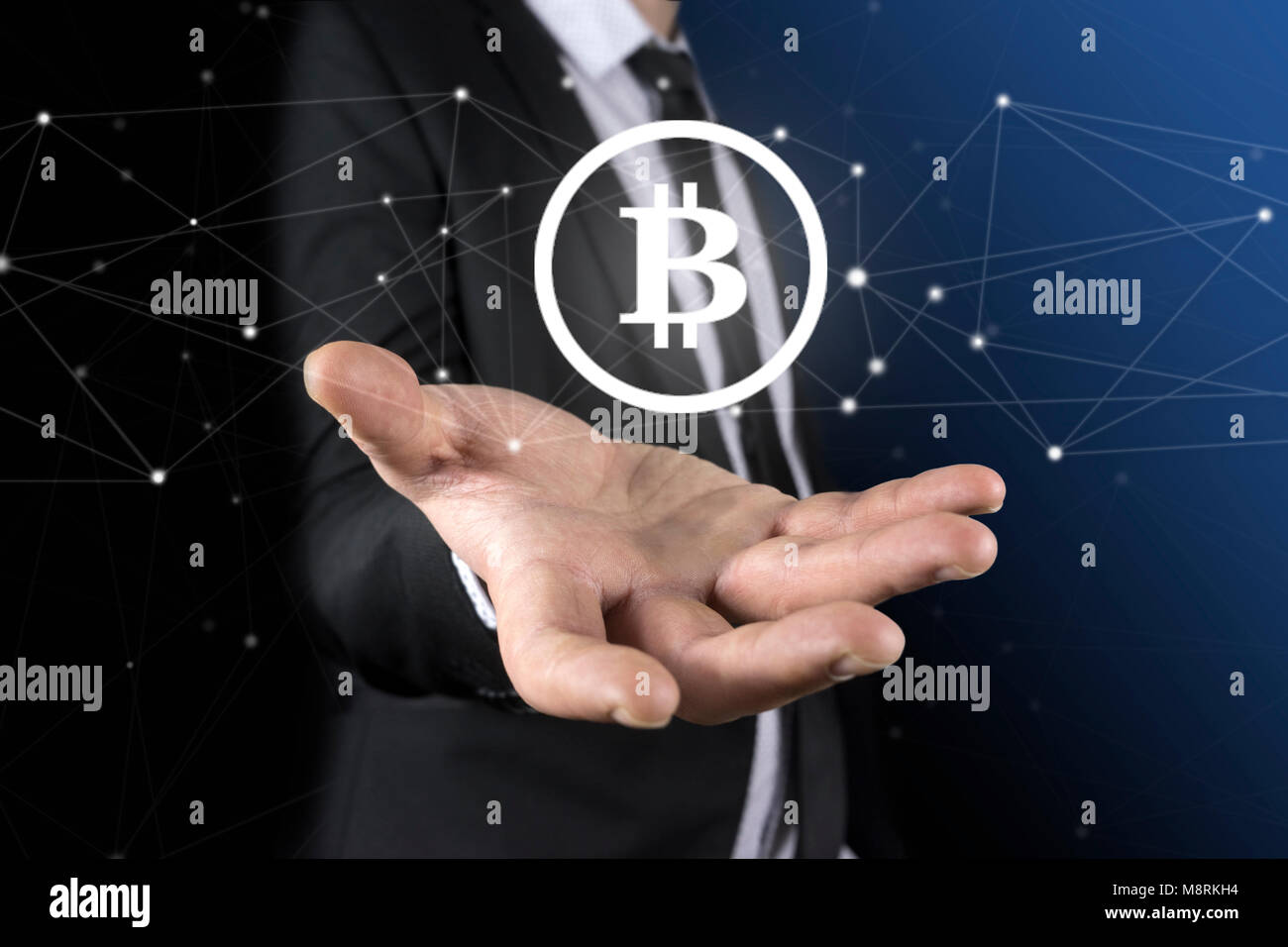 Imprenditore irriconoscibile s mani tenendo un round bitcoin ologramma. A sfocare lo sfondo blu. Foto Stock