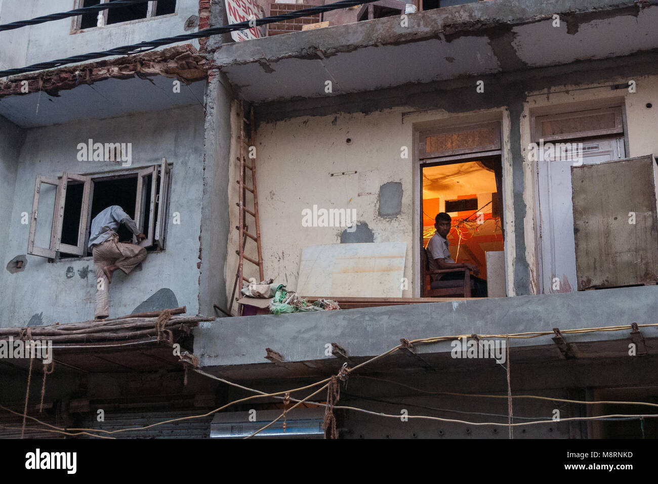 New Delhi, India:In un edificio in fase di ristrutturazione nel Sadar Bazar, un uomo cerca di entrare attraverso la finestra mentre un altro lavora nel suo ufficio. Foto Stock