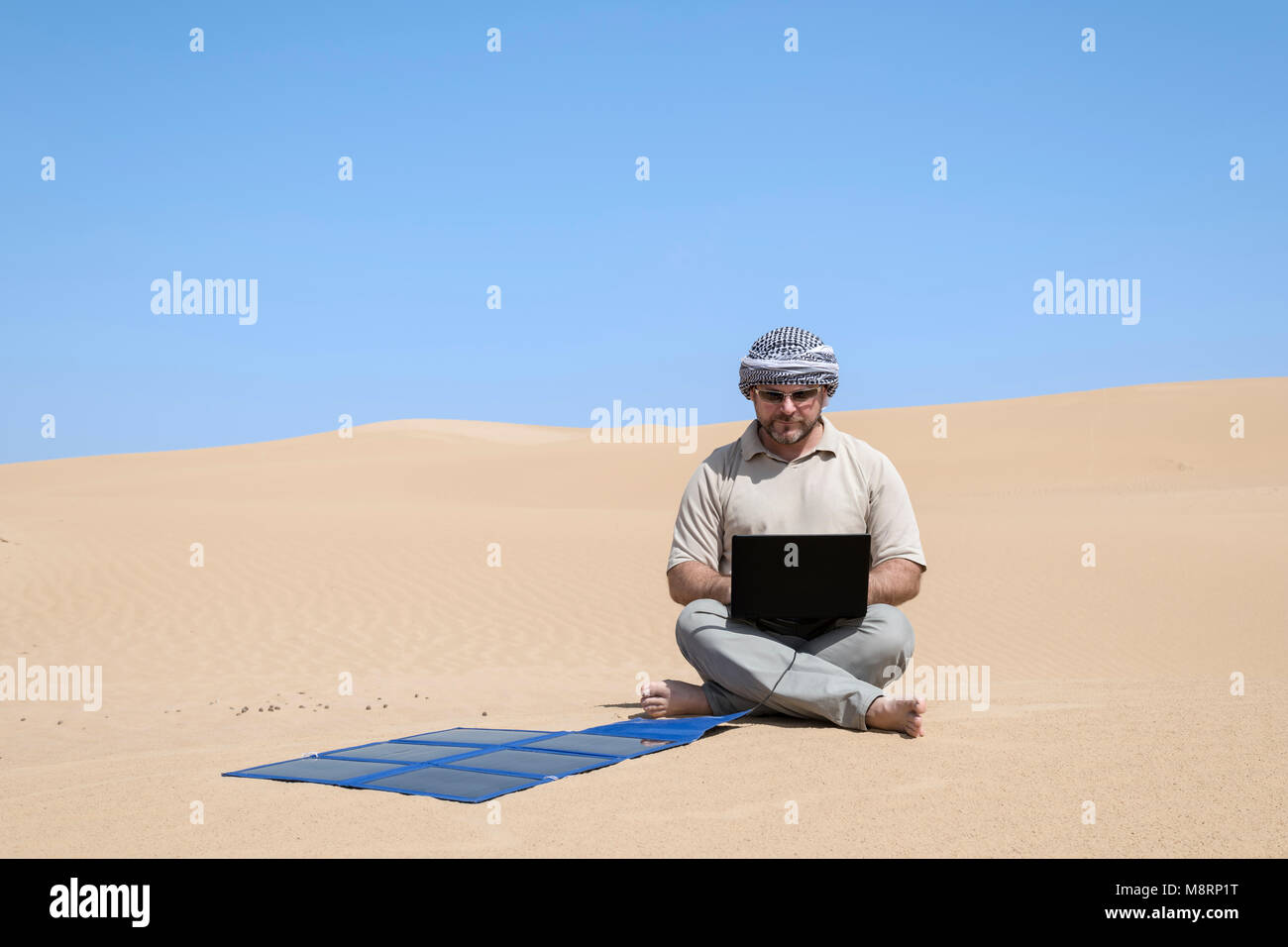 Uomo che lavora con un laptop che si ricarica da un pannello solare portatile all'aperto nel deserto. Lavorare in remoto con gadget, autosufficienza e spazio di copia ecocompatibile Foto Stock