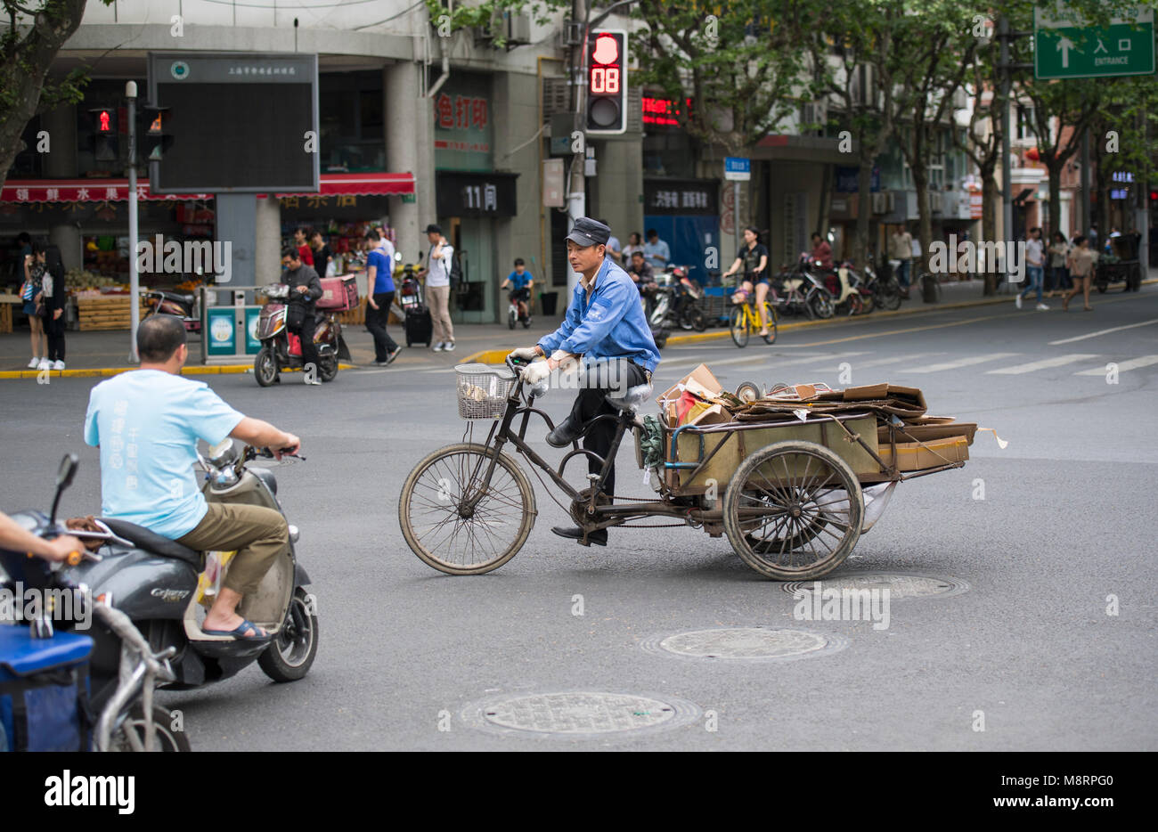 Persone a cavallo delle biciclette e scooter per le strade di Shanghai in Cina Foto Stock