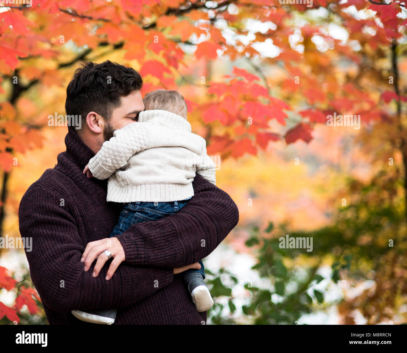 Padre amorevole abbracciando il figlio mentre trasporta lui al parco durante l'autunno Foto Stock