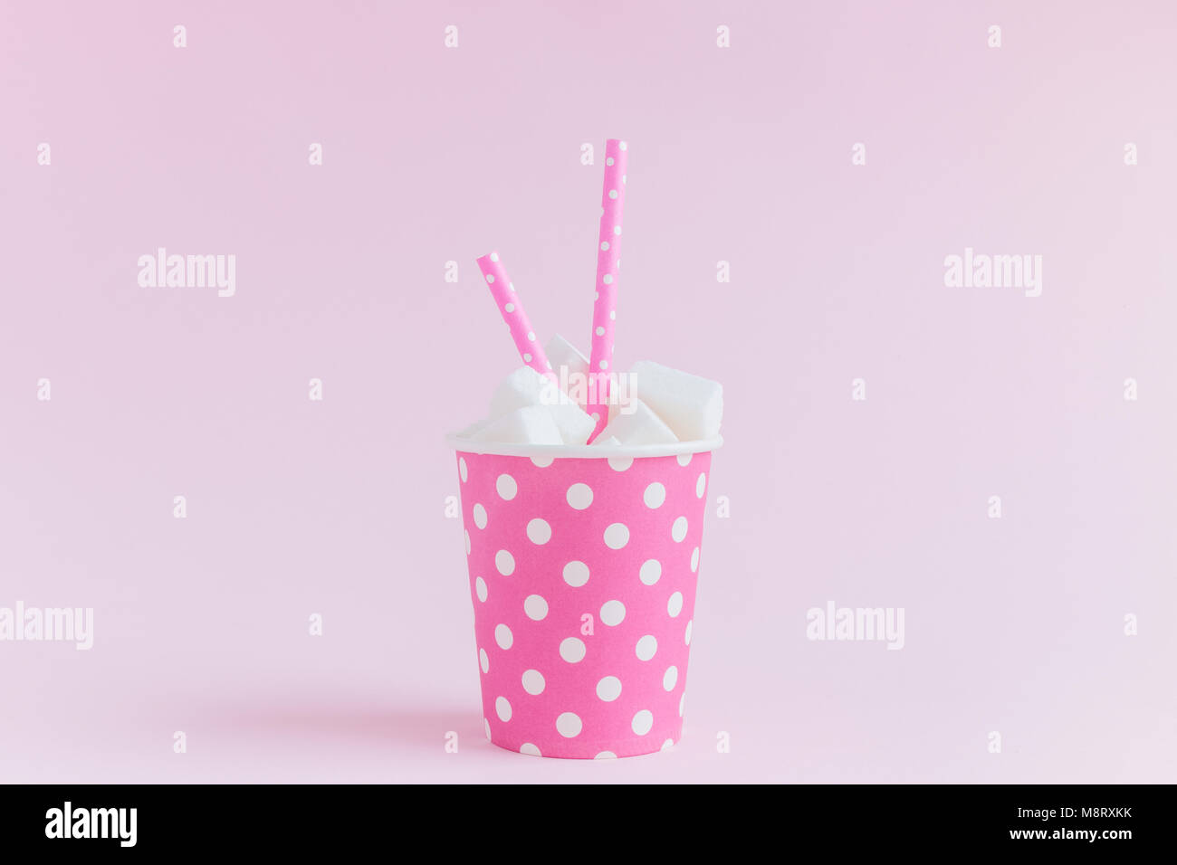 Bicchiere di carta polka design pieno di cubetti di zucchero con acqua potabile cannucce pastello su sfondo rosa la minima nozione. Foto Stock