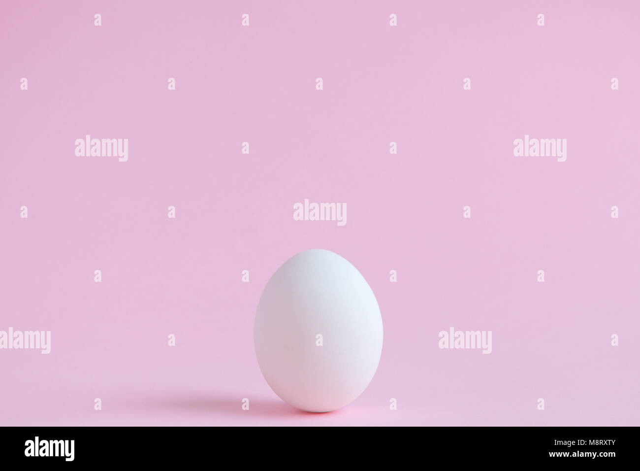 Uovo bianco sulla pianura rosa pastello sfondo. La minima nozione. Foto Stock