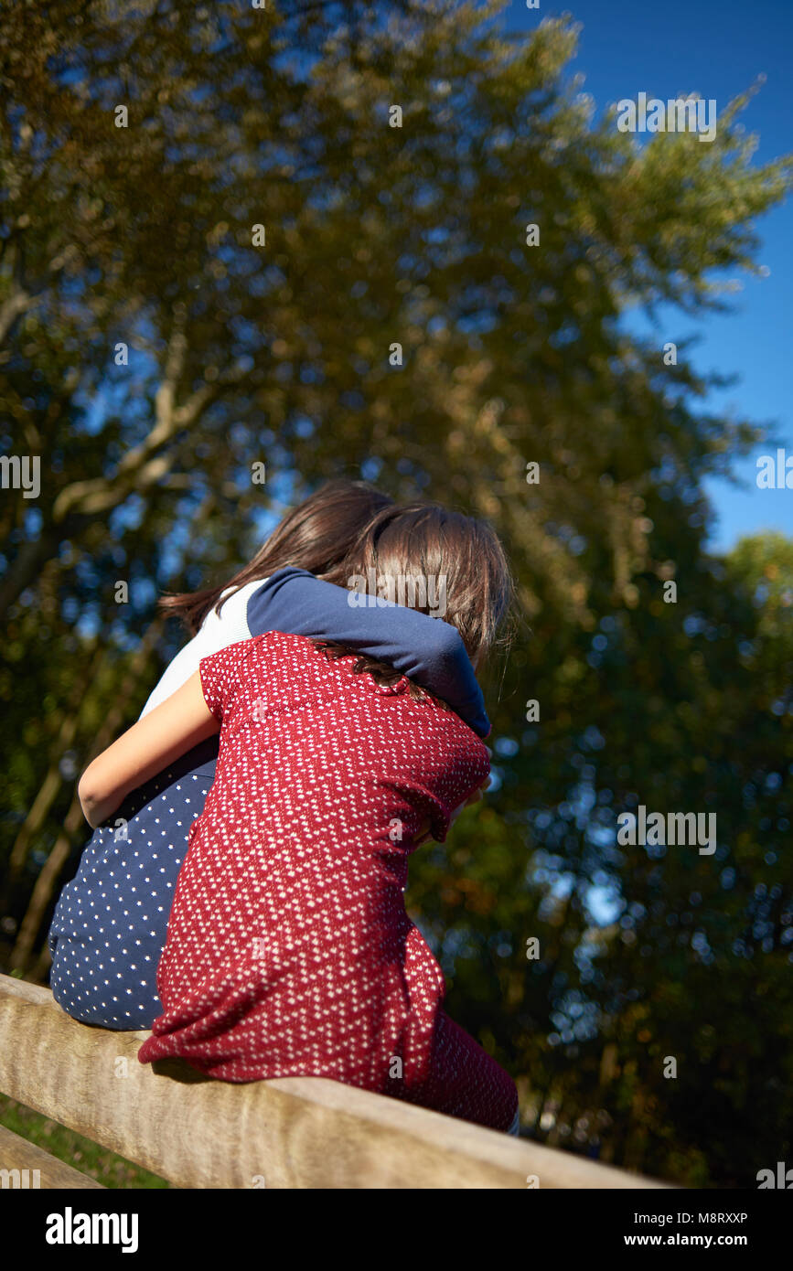 Vista posteriore delle sorelle amici seduti con le braccia intorno a Foto Stock