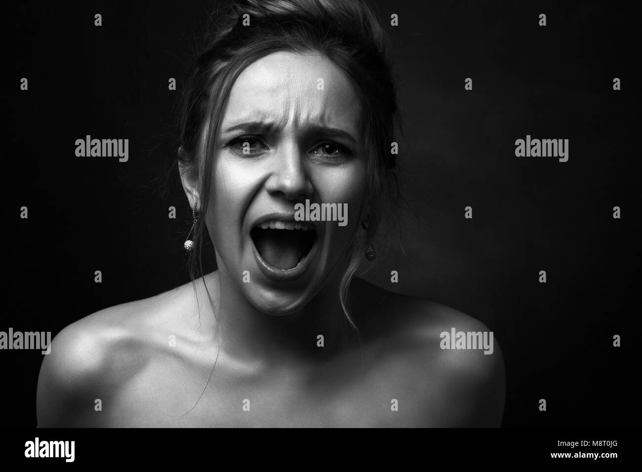 Giovani arrabbiati donna su sfondo nero urlando su telecamera monocromatica Foto Stock