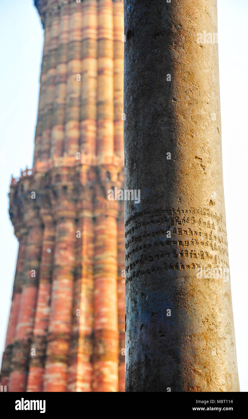 La "Colonna di ferro di Delhi - Close up di antica scritta in sanscrito sulla corrosione-libera la colonna della vittoria, sovrapposti contro la Qutub Minar minareto. Foto Stock