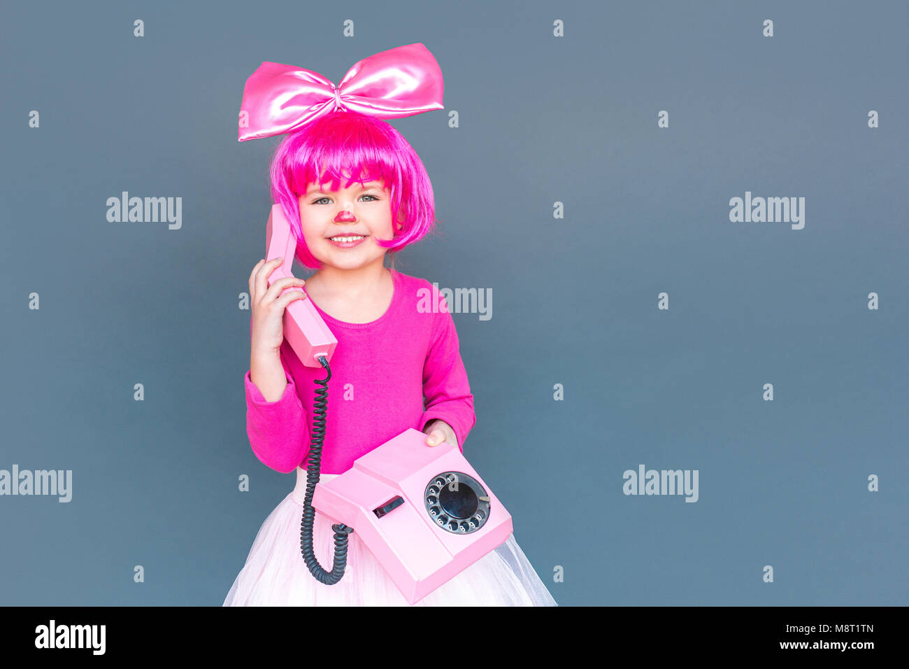 Ritratto di poco il clown girl chiamando sul vecchio telefono rosa, toothy sorridente. Studio shot, isolata su uno sfondo grigio Foto Stock