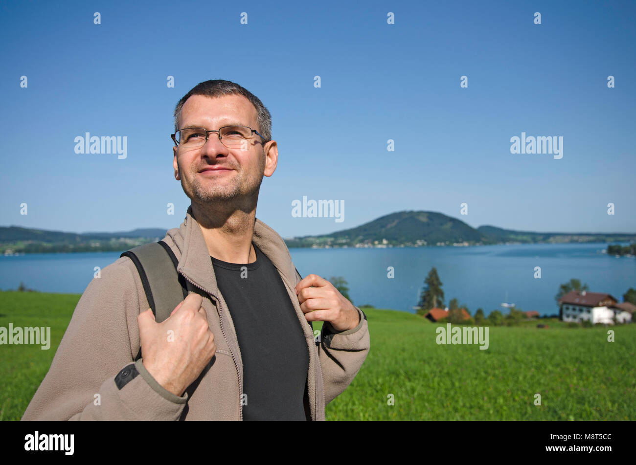Un turista con lo zaino escursionismo su una strada di campagna vicino al lago. Una piccola città e il verde delle colline in background Foto Stock