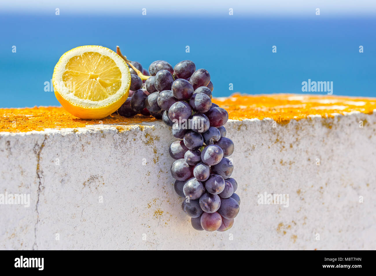 Mezzo limone e il grappolo di uva blu sulla parete vicino al mare Foto Stock