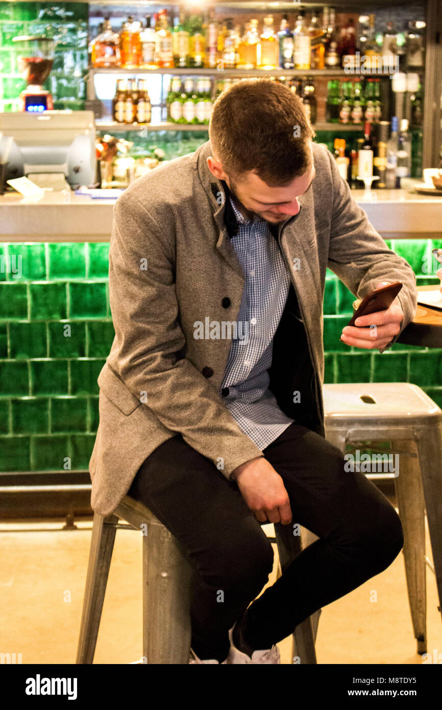 Uomo in attesa in un bel bar con telefono cellulare, REGNO UNITO Foto Stock