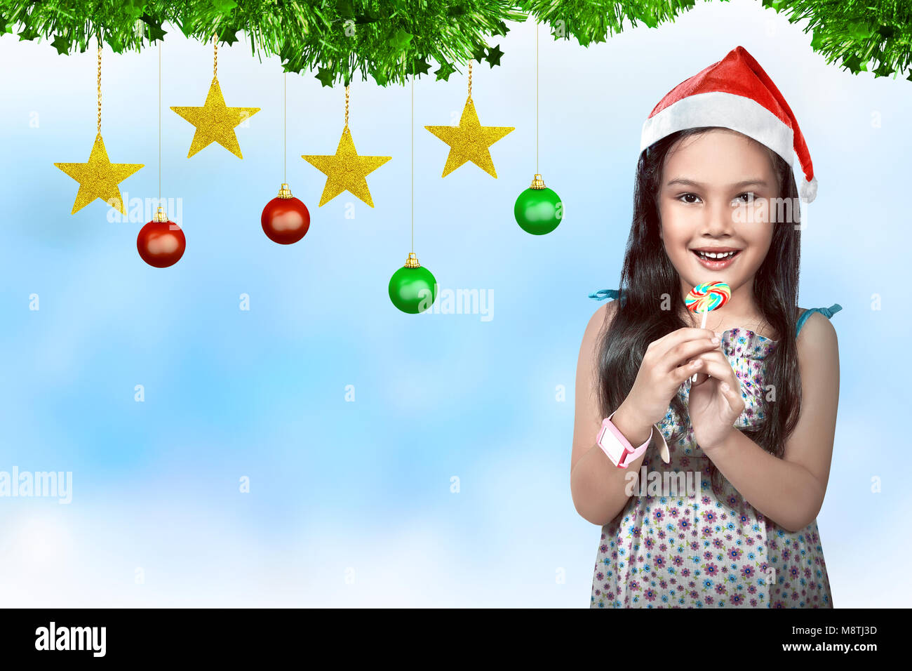 Carino asian bambina indossa santa hat con decorazione natalizia sullo sfondo. Natale in luglio Foto Stock