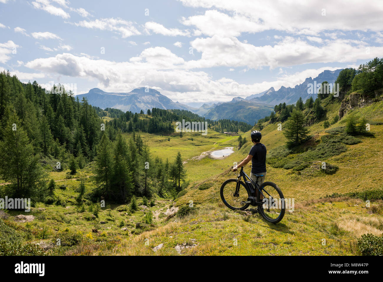 Giovane adulto uomo attivo sulla montagna di indossare il casco protettivo guardando il suggestivo panorama azienda elettrica bici nella soleggiata giornata estiva all'aperto. Foto Stock