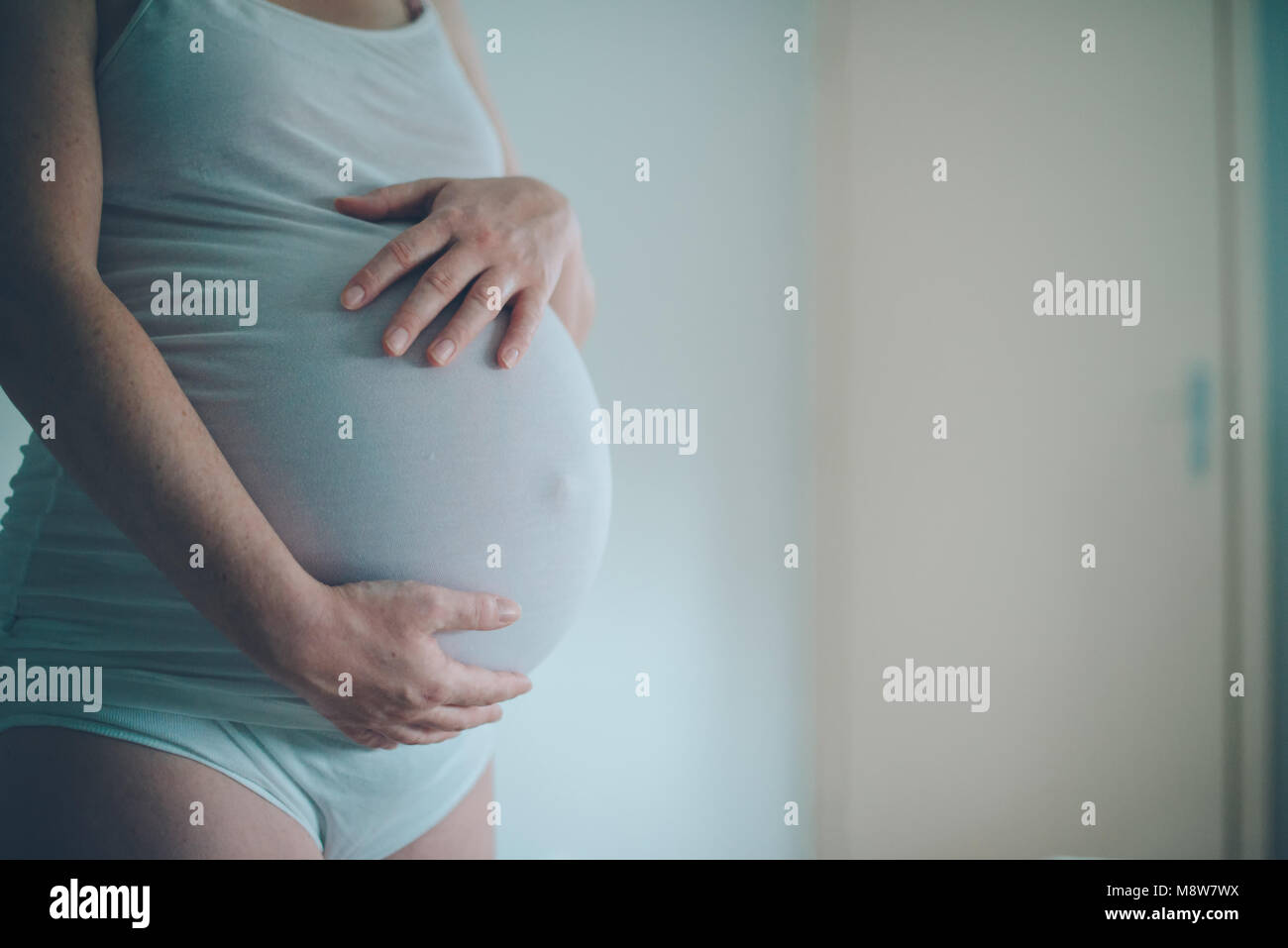 Donna incinta cuddling pancia in camera da letto a casa appena prima che il travaglio e il parto, il fuoco selettivo Foto Stock