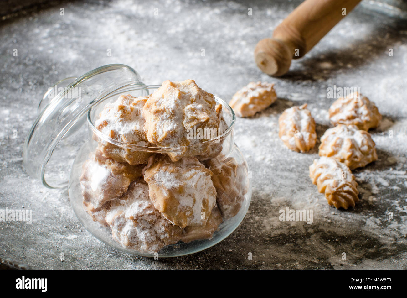Confetti i biscotti con lo zucchero in polvere nel recipiente di vetro e del rullo di pasta. Polvere di metallo scuro dello sfondo Foto Stock