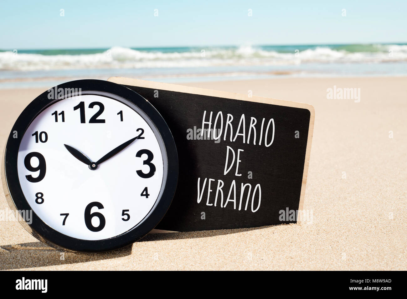 Primo piano di un orologio e di un cartello con scritto il testo horario de verano, estate tempo scritto in spagnolo, sulla sabbia di una spiaggia Foto Stock