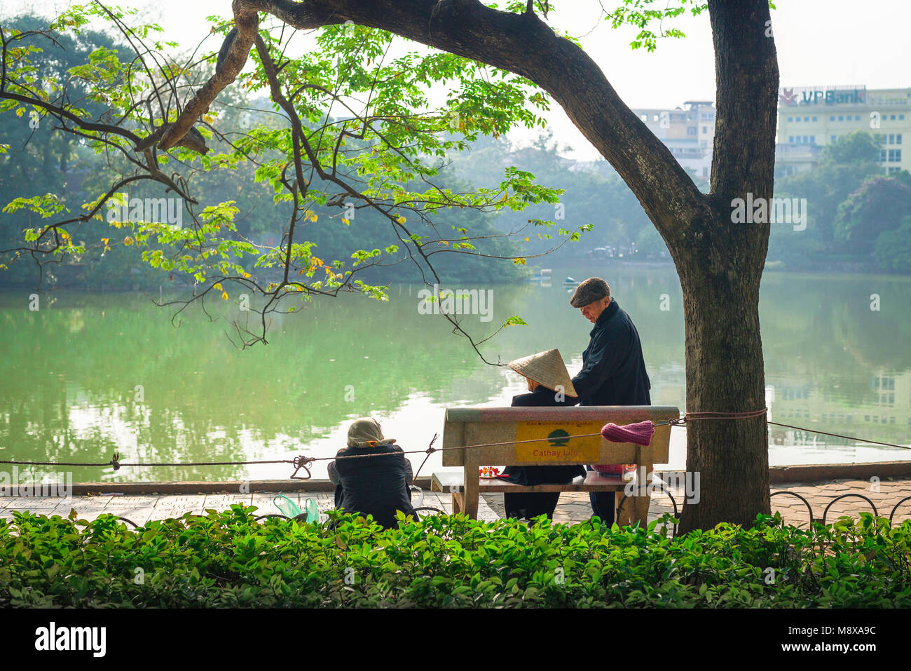 Vietnam, vista posteriore dei cittadini anziani di Hanoi che si godono il sole primaverile sul lago Hoan Kiem, Vietnam. Foto Stock
