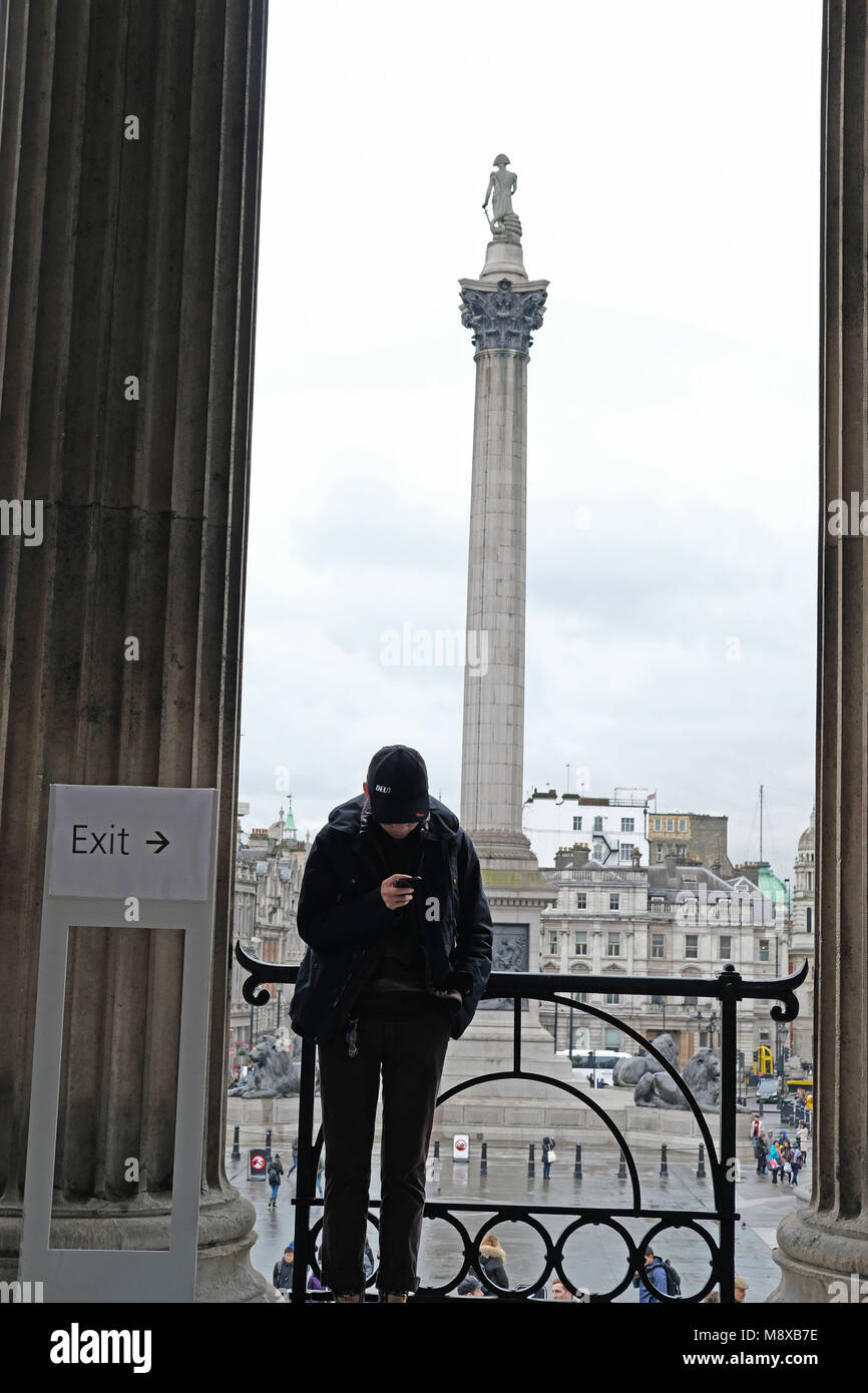 Un turista sul suo telefono con Nelsons Column in background. Foto Stock