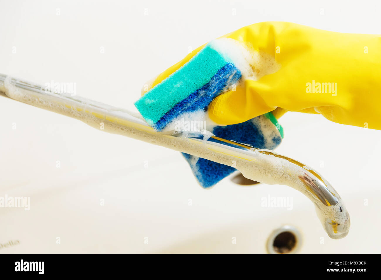 Bagno di pulizia rubinetto con detergente in giallo guanti in gomma con spugna blu - Lavori Domestici pulizie di primavera Concept Foto Stock