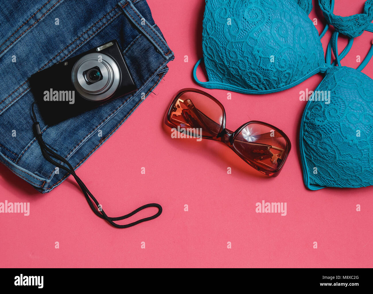 Costume da bagno, Jeans, occhiali da sole, foto fotocamera su sfondo rosa. Vista dall'alto concetto di viaggio con Copyspace Foto Stock