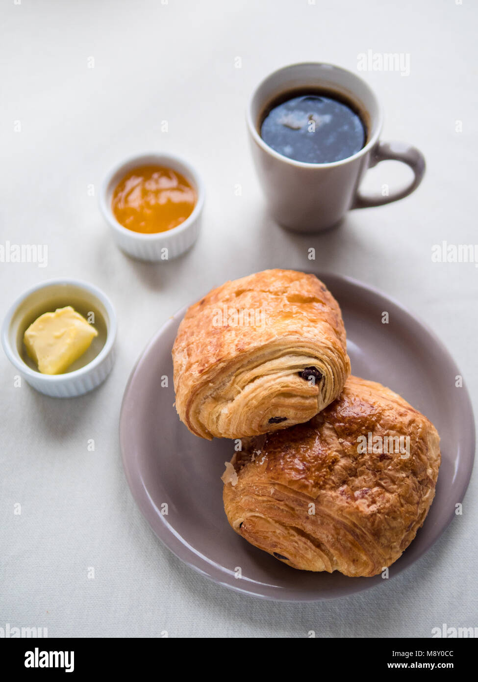 Vista al di sopra di una prima colazione continentale con il francese croissant al cioccolato, burro, marmellata e caffè nero su bianco nella tabella Foto Stock