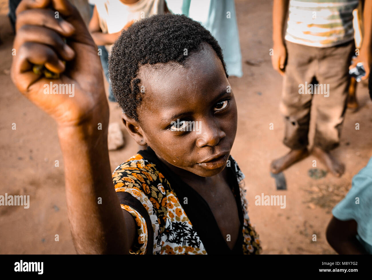 Un africano colorati bambino chiede aiuto come egli è ritratto intensamente fissando la lente della fotocamera, in un villaggio nei pressi di Watamu, Kenya, Africa Foto Stock
