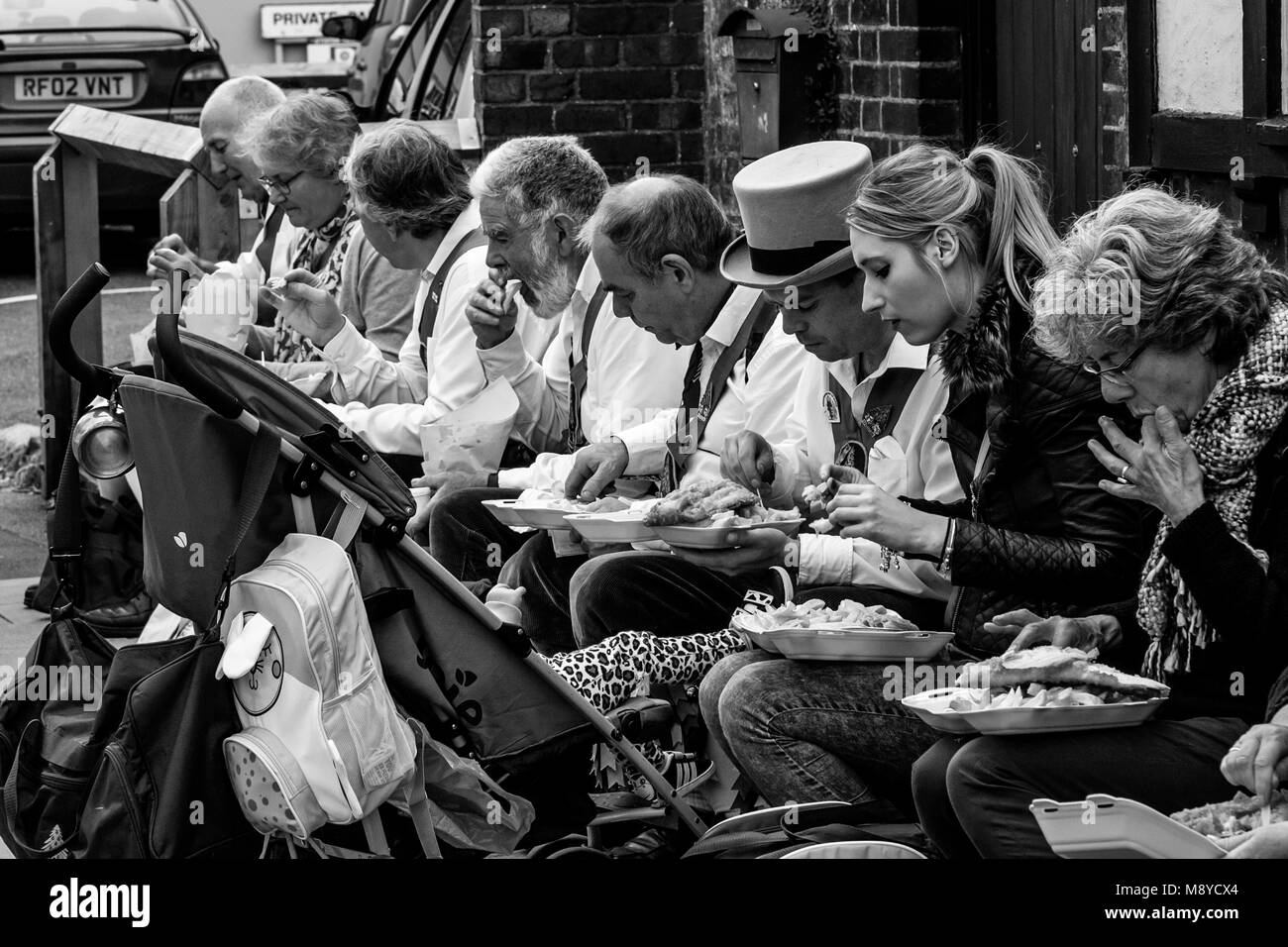 Un gruppo di ballerini di Morris a sedersi su una parete di mangiare pesce e patatine durante l annuale Lewes Folk Festival, Lewes, Sussex, Regno Unito Foto Stock