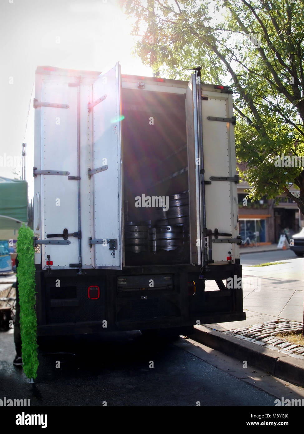 Una collezione di argento barili di birra impilate insieme nella parte posteriore di un carrello aperto parcheggiata in corrispondenza di un cordolo di città con il tardo pomeriggio di sole attraverso lo streaming. Foto Stock