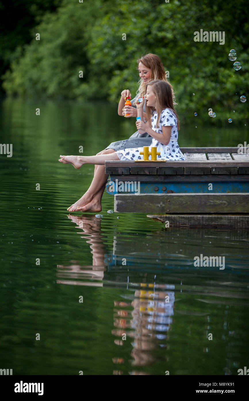 Madre e figlia soffiando bolle di sapone in riva al lago Foto Stock