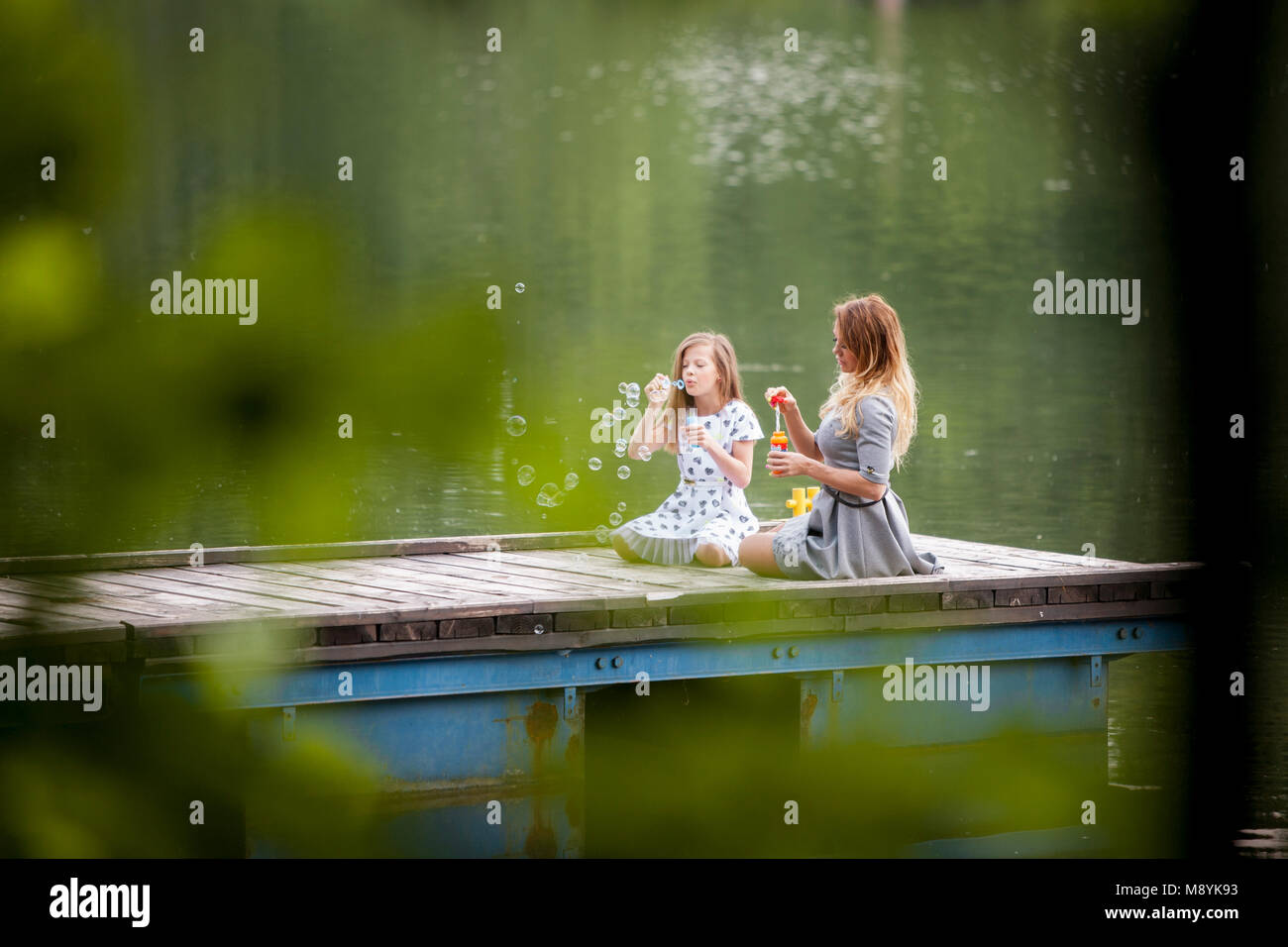 Madre e figlia soffiando bolle di sapone in riva al lago Foto Stock