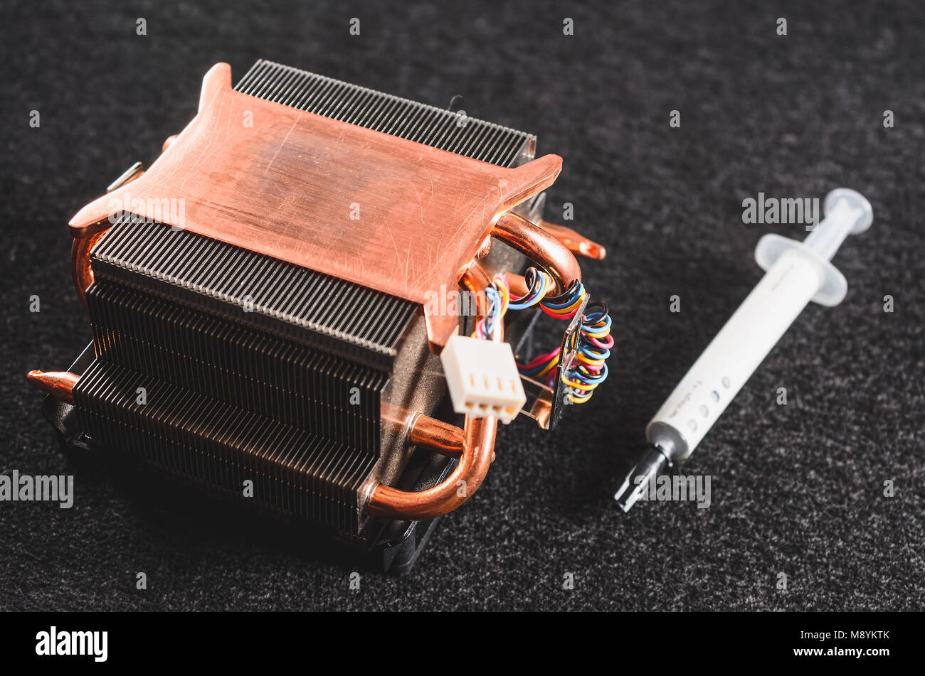 CPU platina di calore da un PC e un grasso termico. Heatsinker di rame con una ventola di raffreddamento del processore. Focus sul dissipatore, isolato su un buio indietro Foto Stock