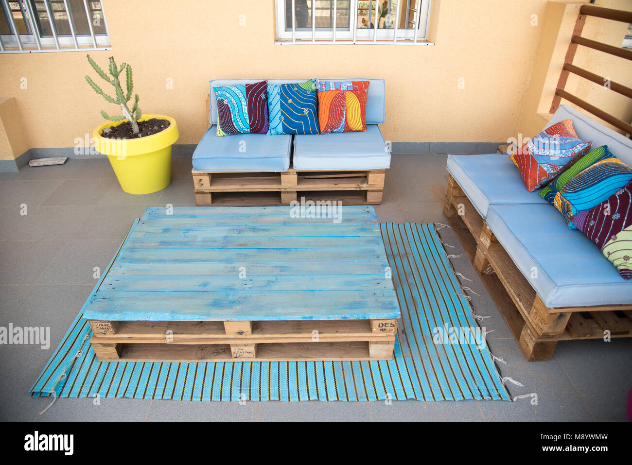 Fresco patio mobili realizzati con le palette di legno. Dipinto di blu con grassetto, colorato tessuto africano cuscini. Luminosa e felice spazio. Foto Stock
