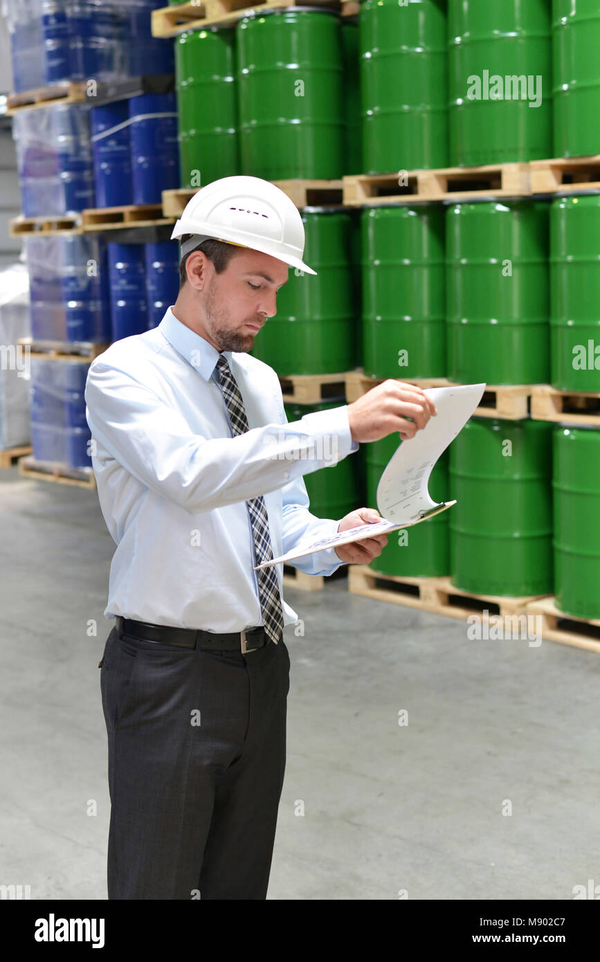 Manager di una società di logistica lavorare in un magazzino con prodotti chimici - controllare le merci con clipboard Foto Stock