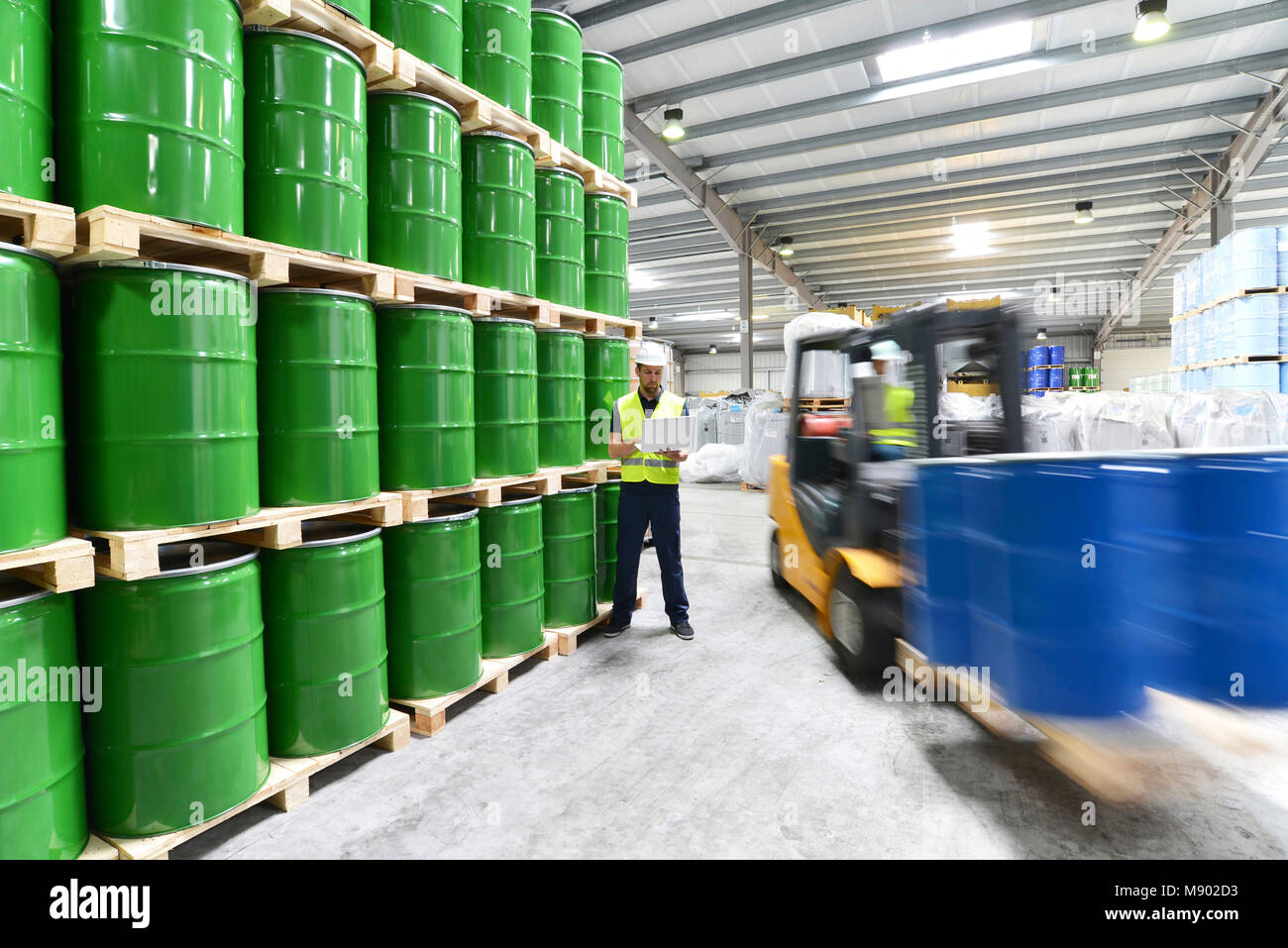 Gruppo di lavoratori con elevatore a forche nell'industria logistica lavorando in un magazzino con barili di chimica Foto Stock