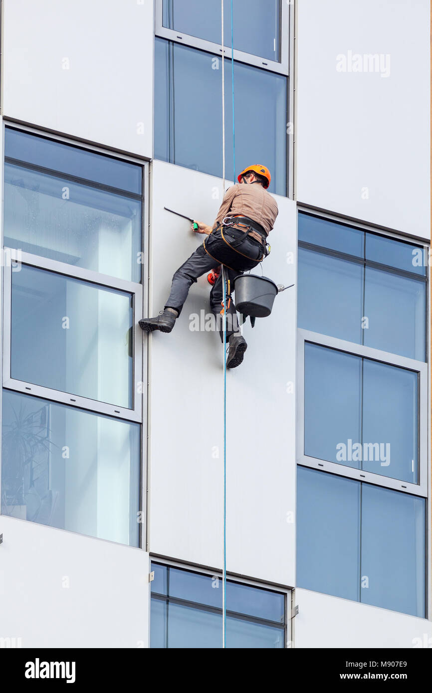 Il lavoratore appeso sulla corda clambing, pulire le finestre ond guscio esterno dell'edificio alto. Foto Stock