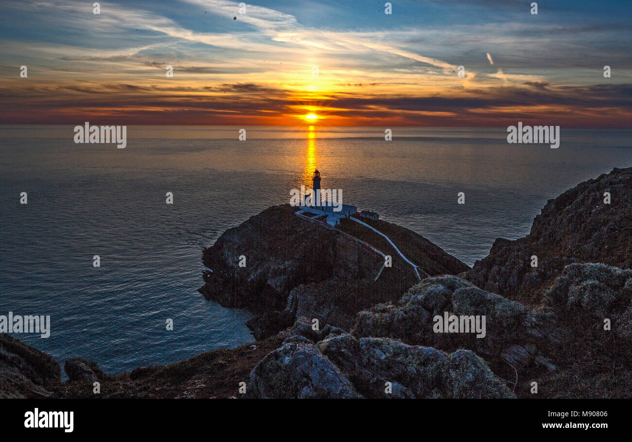 Il sole tramonta dietro il South Stack Lighthouse ad Anglesey, nel Galles del Nord, mentre le condizioni ghiacciate portate dalla 'Bestia dei pini dall'Oriente' sono destinate ad aggrapparsi ancora un giorno prima che la Gran Bretagna possa vedere il ritorno della primavera. Foto Stock