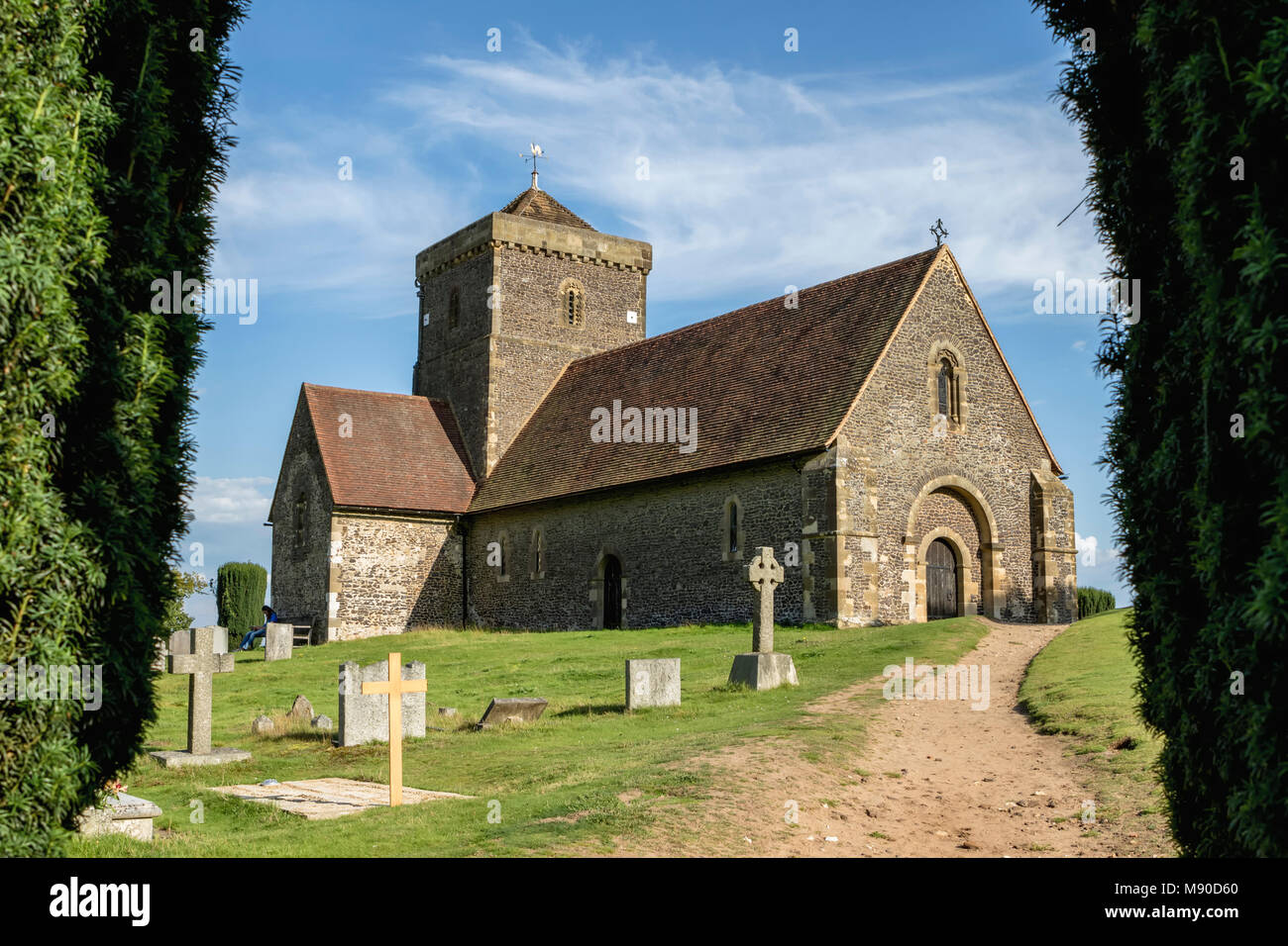 Vista incorniciata di approccio della chiesa e cimitero di St Martha's Hill in una giornata di sole con percorso naturale e alberi sfoltiti Foto Stock