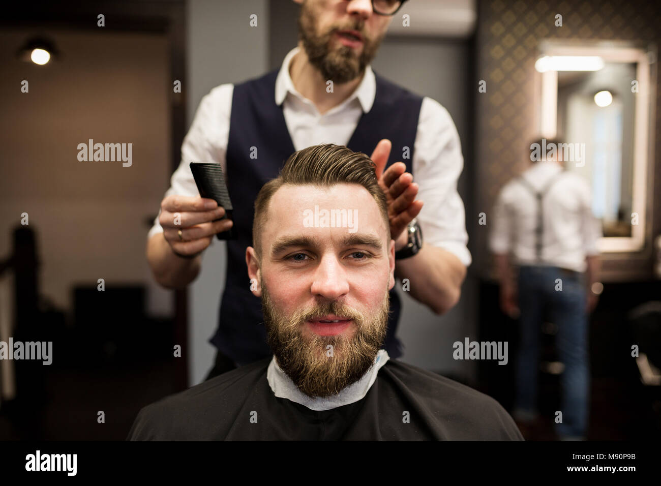Ritratto frontale di lieta giovane uomo avente taglio capelli al Barbiere Salone di bellezza Foto Stock