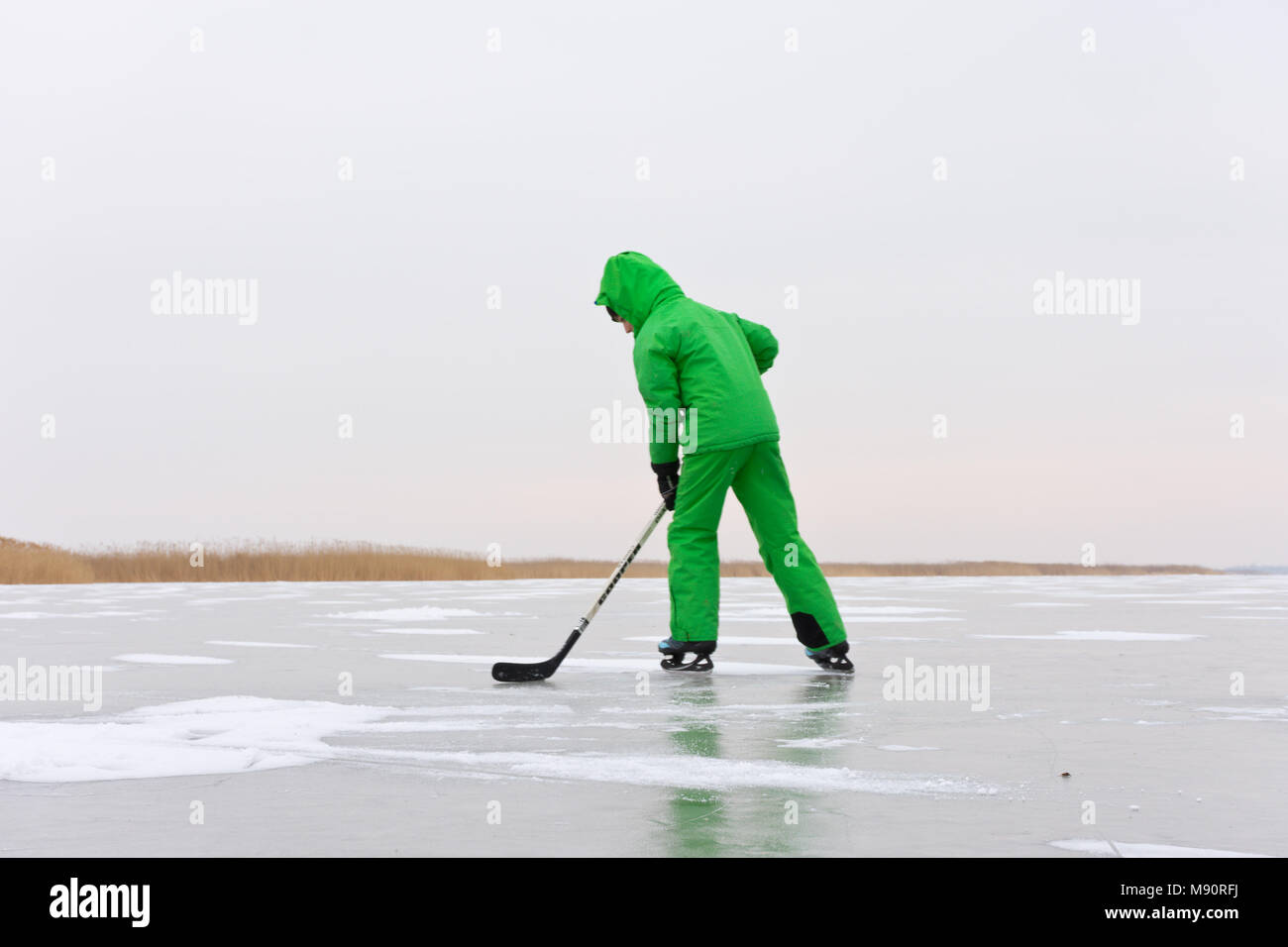 Hockey su ghiaccio giocatore in verde nel complesso sulla spaziosa il ghiaccio naturale superficie del lago ghiacciato di Neusiedl sfidando scialbo nuvoloso e freddo inverno. Foto Stock