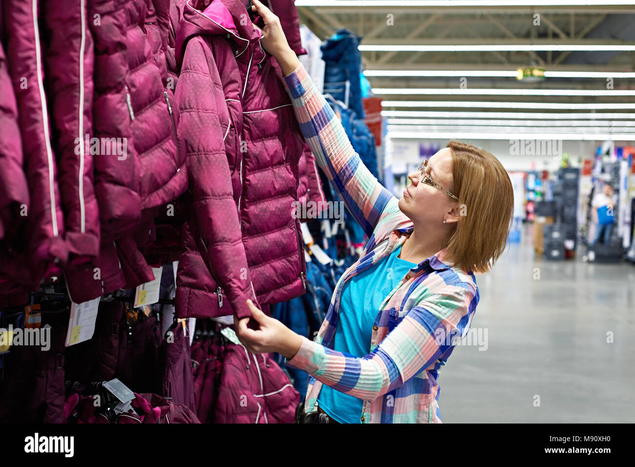 La donna sceglie una giacca invernale in negozio Foto Stock