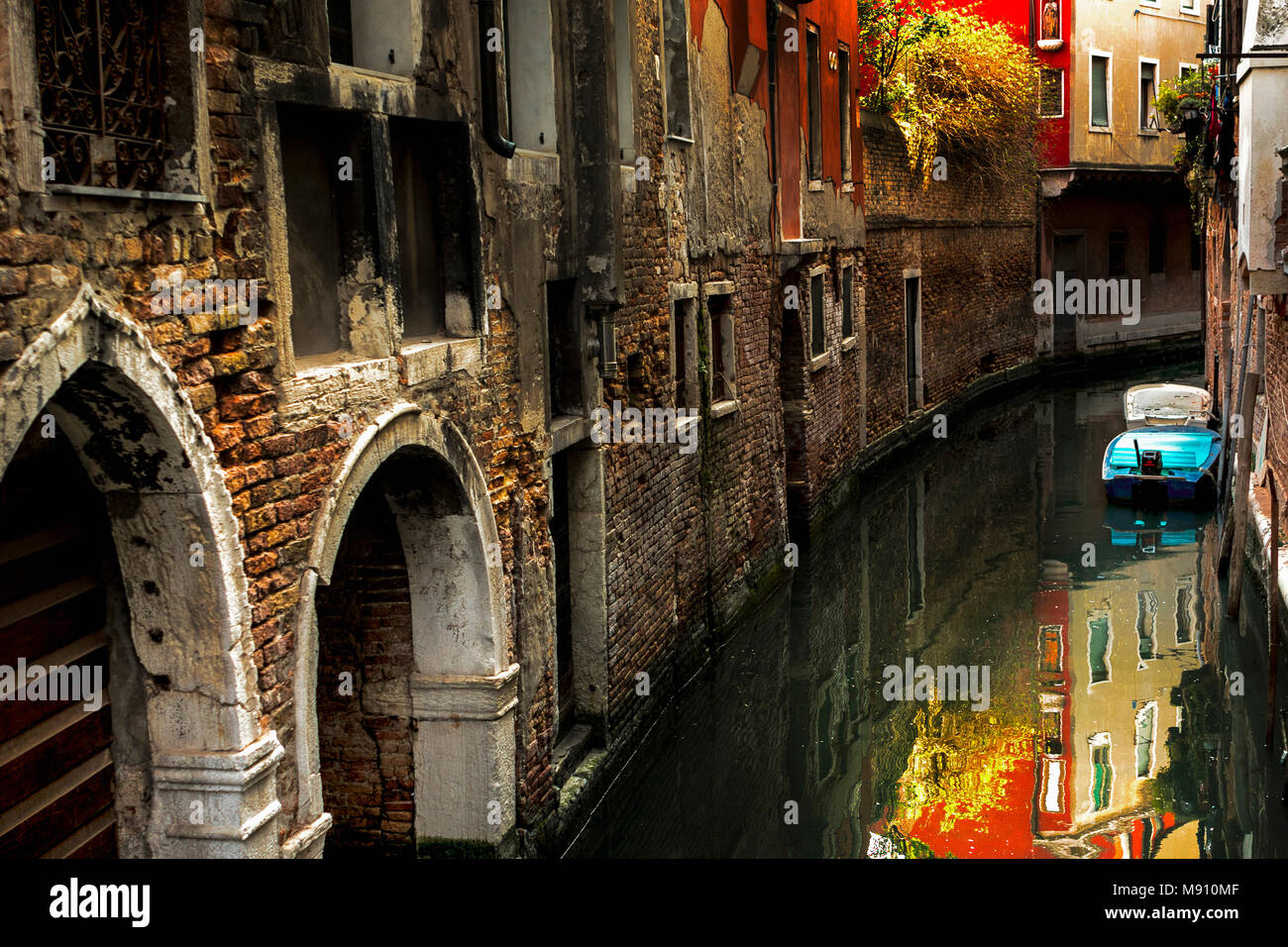 Stretto canale ombreggiato percorso di decadimento vecchi muri di mattoni evoluzione del fogliame soleggiato riflettendo in acqua e pitturato di bianco arcate e cenge in Venezia Foto Stock