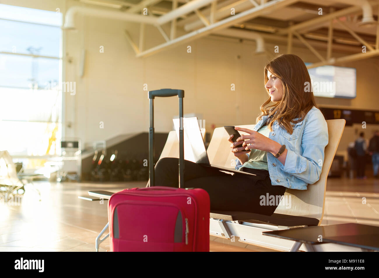 Aeroporto femmina giovane passeggero su smart phone e il computer portatile seduti nella sala terminale durante l'attesa per il suo volo Foto Stock