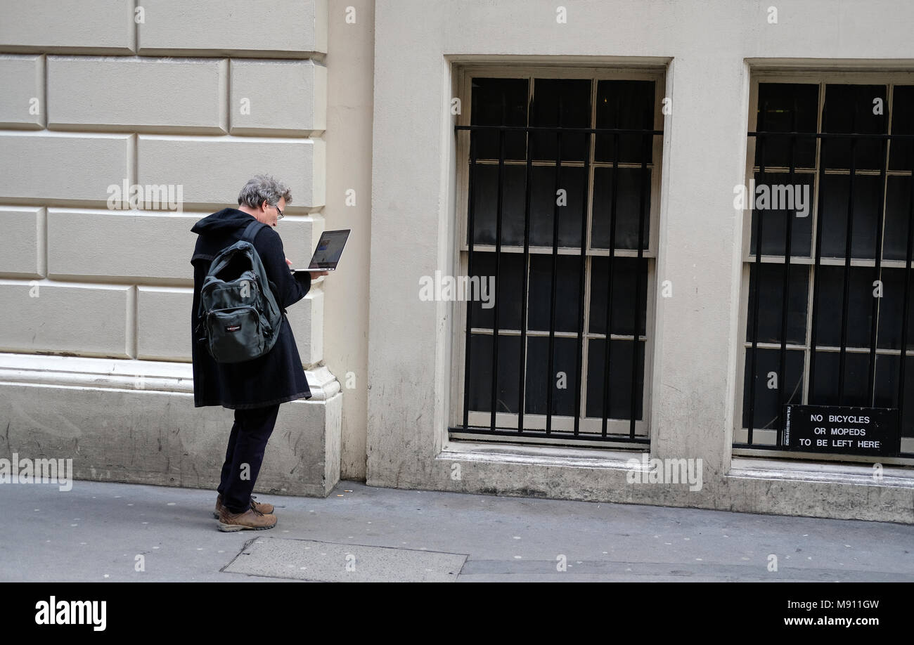 Un uomo che guarda il suo computer portatile su una strada di Londra. Foto Stock
